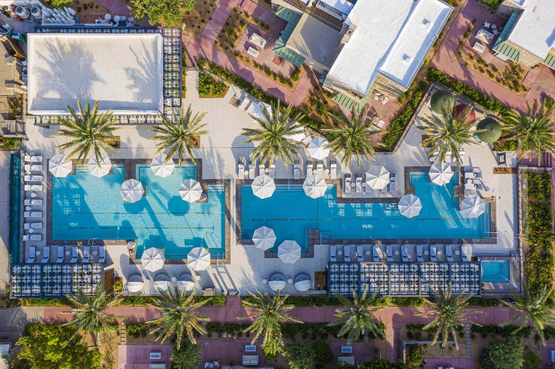 Aerial view of a rectangular swimming pool surrounded by palm trees, lounge chairs, and white umbrellas in a landscaped resort setting—an inviting oasis perfect for celebrating Labor Day Weekend in Phoenix.